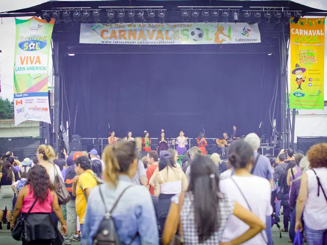 In this image there is a stage with the blue color curtain. There are banners. There are people...