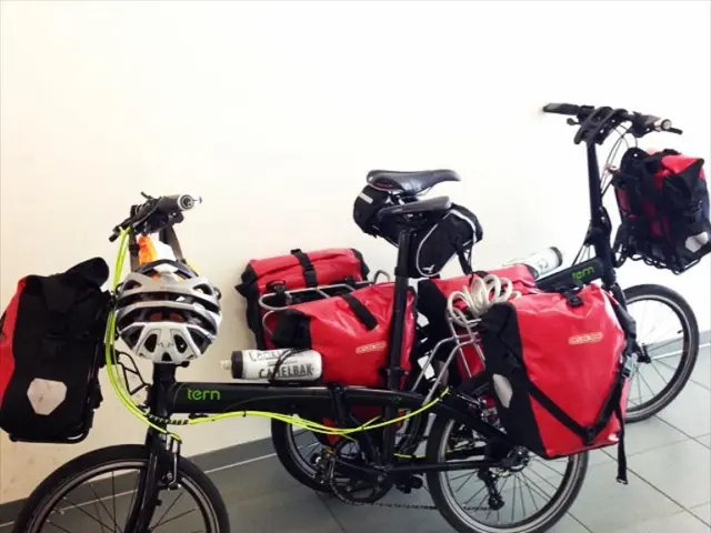 In this image we can see the bicycles near the wall. And there are bags and helmets attached to the...